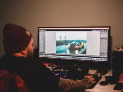 Unrecognizable tattooed male sitting at table and working on computer with montage video of sport car