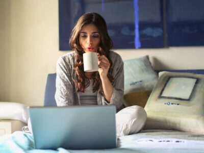 Woman in Grey Jacket Sits on Bed Uses Grey Laptop